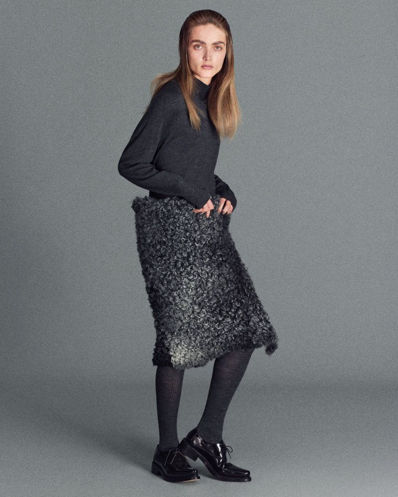 Model wearing a dark grey sweater and textured skirt against a grey background