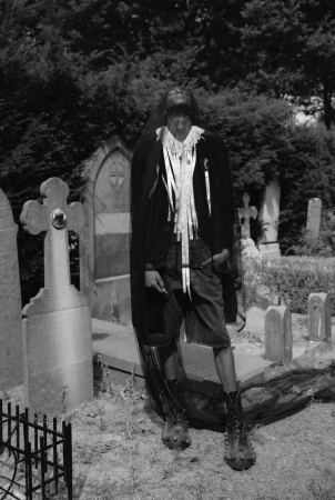 Model wearing a black veil and dark attire standing in a cemetery among stone headstones for HERO Magazine