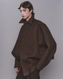 Model wearing a structured brown checkered coat with a high collar against a grey background