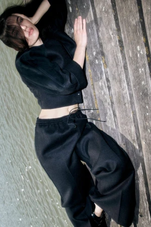 Woman in black long-sleeve top and trousers lying on a wooden pier next to water