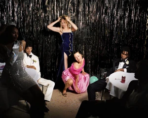 Group of people in formal attire posing in front of a shiny dark fringe backdrop for W Youth editorial.