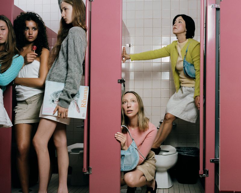 Group of women posing inside a public restroom with pink stall doors and white tiled walls.