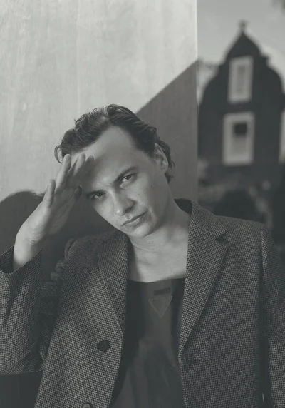 Portrait of actor Frank Dillane wearing a patterned blazer with his hand raised to his forehead, photographed by Carmine Romano for Crash Magazine.