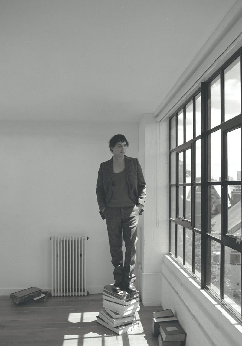 Actor Frank Dillane standing on a stack of books by a large grid window in a bright room for Crash Magazine