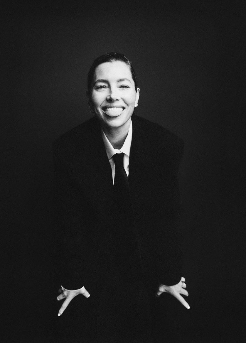 Jessica Biel in a black suit and tie smiling against a dark background for M Revista de Milenio