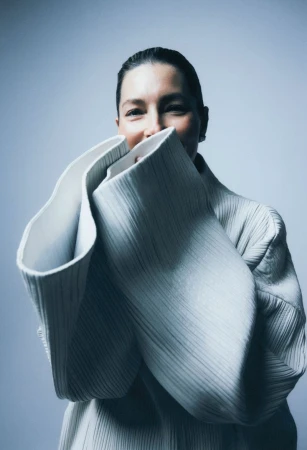 Jessica Biel wearing a sculptural textured white garment with oversized flared cuffs against a plain grey background