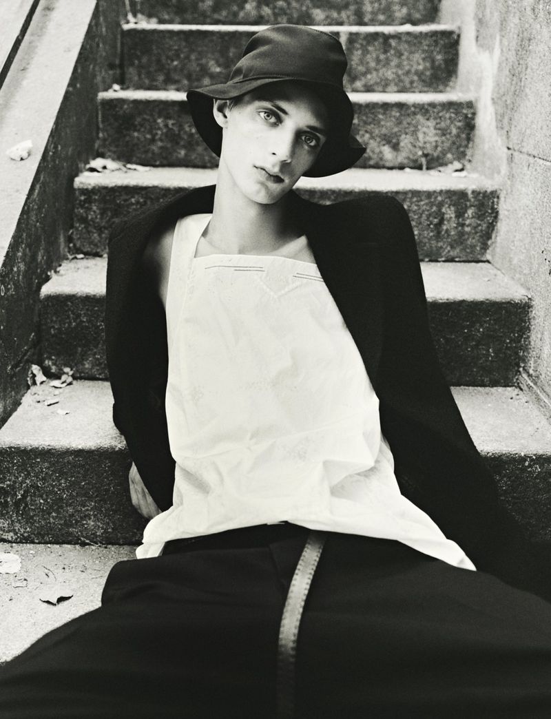 Model wearing a black bucket hat and white top seated on outdoor stone stairs for HERO Magazine editorial