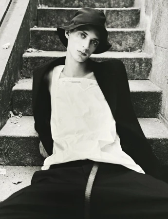 Model wearing a black bucket hat and white top seated on outdoor stone stairs for HERO Magazine editorial