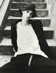 Model wearing a black bucket hat and white top seated on outdoor stone stairs for HERO Magazine editorial