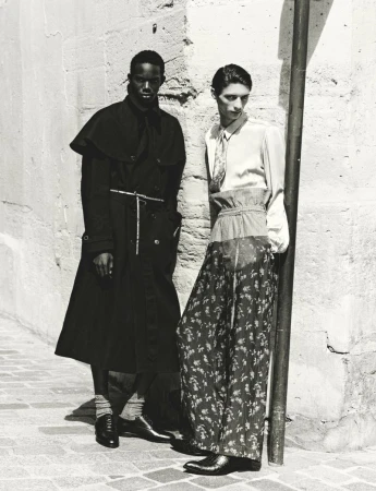 Two male models posing outdoors against a textured stone wall in black and white fashion editorial photography