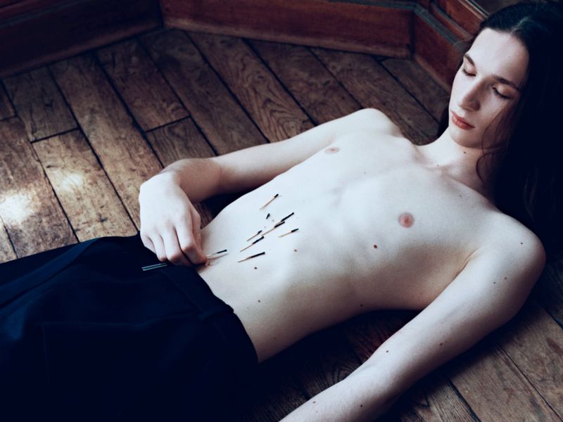 Shirtless person lying on a wooden floor with matches arranged on their abdomen for HERO Magazine