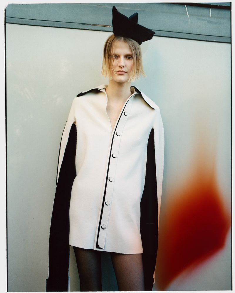 Portrait of a fashion model in a white button-down shirt with black sleeves and a star headpiece, posing in front of a studio wall.