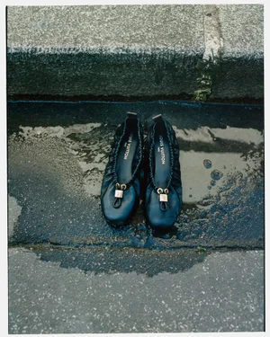 A pair of black leather ballet flats resting in a puddle beside a concrete curb for the WRPD Magazine editorial Satin Roads.