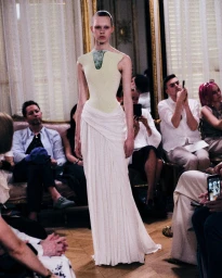 Model walking the runway in a pale green and white sculptural haute couture gown during a fashion presentation.