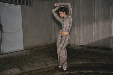 Zendaya wearing a patterned long-sleeve top and trousers posing on stone steps against a concrete wall