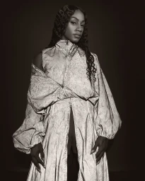 Portrait of Sha'Carri Richardson wearing a structured grey patterned jacket against a dark background for Nike Atelier.