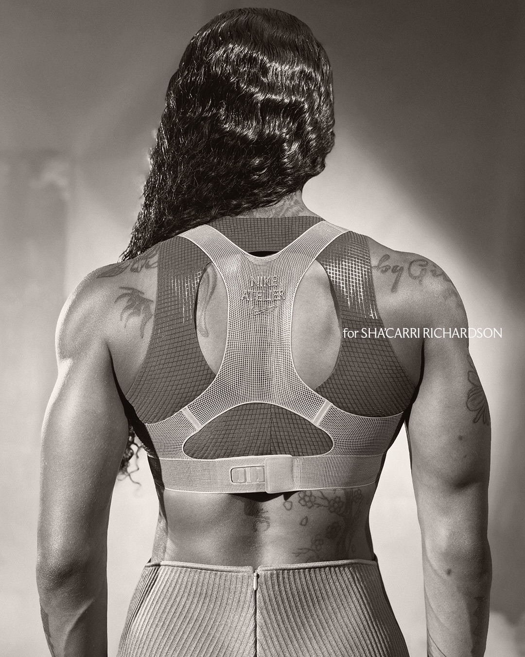 Rear view of Sha'Carri Richardson wearing a Nike Atelier athletic top with tattoos visible on her back and shoulders.