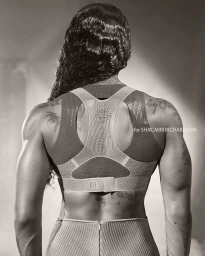 Rear view of Sha'Carri Richardson wearing a Nike Atelier athletic top with tattoos visible on her back and shoulders.