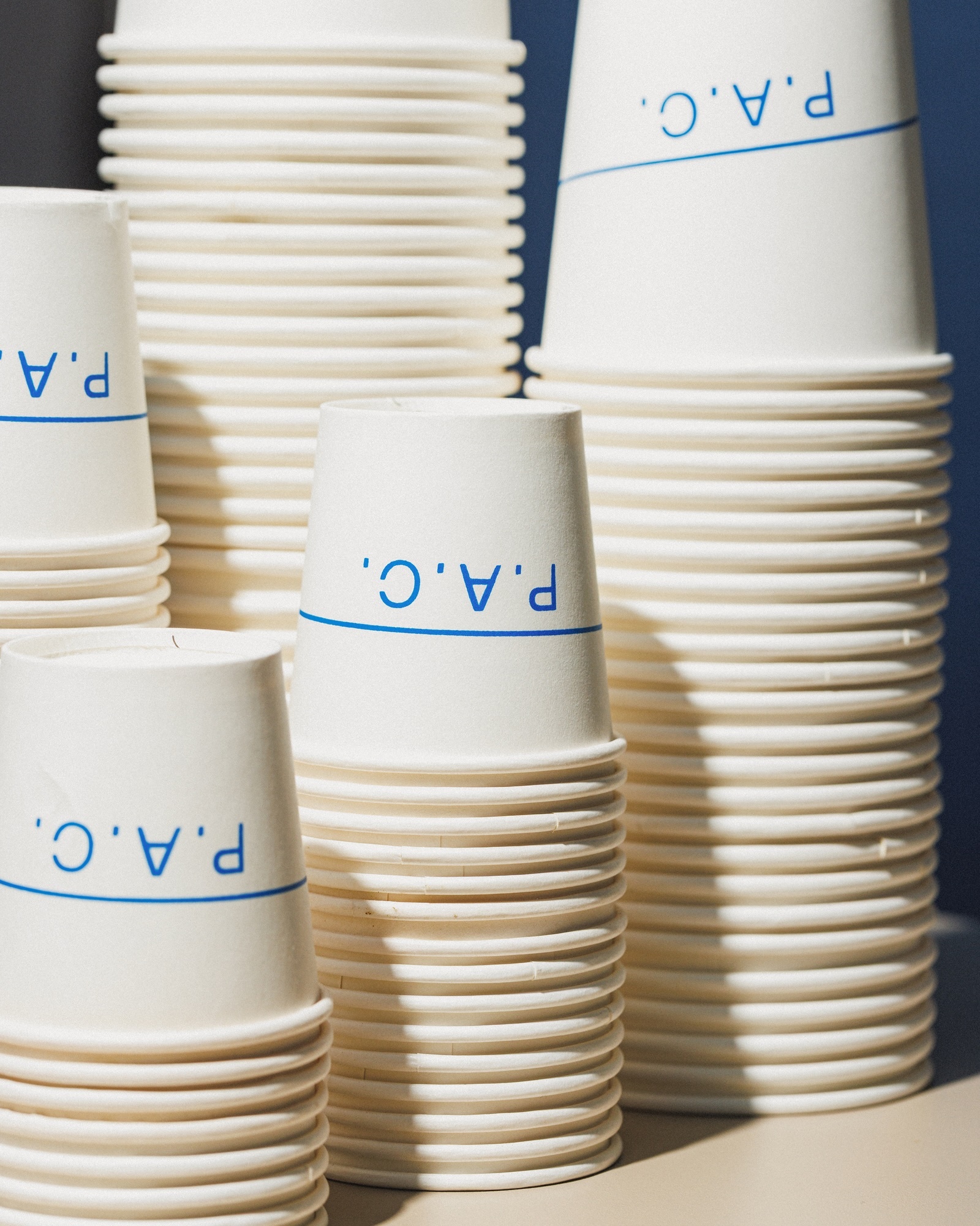 Stacks of white paper cups with blue logo printing arranged in a composition against a neutral background