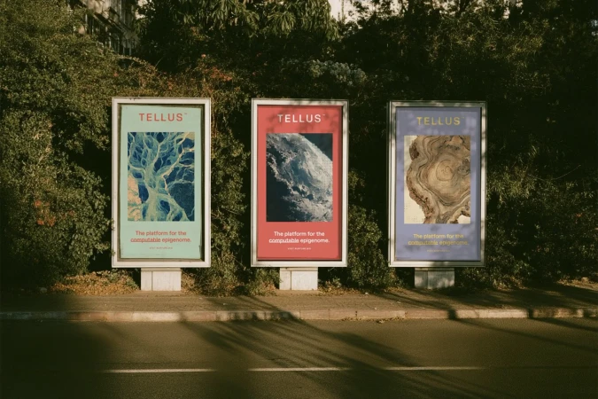 Three outdoor advertising lightboxes displaying branding for Tellus positioned along a curb with dense foliage behind.