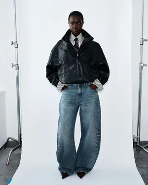 Model wearing a black leather jacket and blue denim jeans standing in a white seamless photography studio