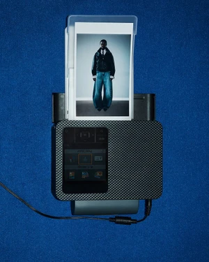 Compact portable printer resting on a textured blue surface displaying a printed photograph of a fashion model