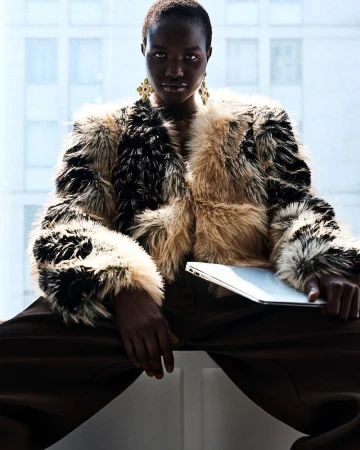 Model Akon Changkou wearing a fluffy patterned jacket and holding a laptop against an office window backdrop