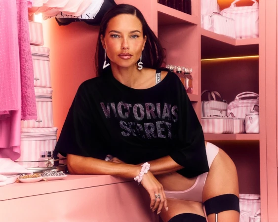 Model Adriana Lima wearing a black t-shirt and pink underwear in a pink retail showroom setting