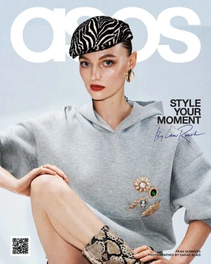 Model wearing zebra-print beret and grey hoodie adorned with jewelled brooches against a neutral studio background
