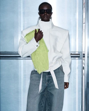 Model in white high-neck jacket and sunglasses holding a bright green fringed bag
