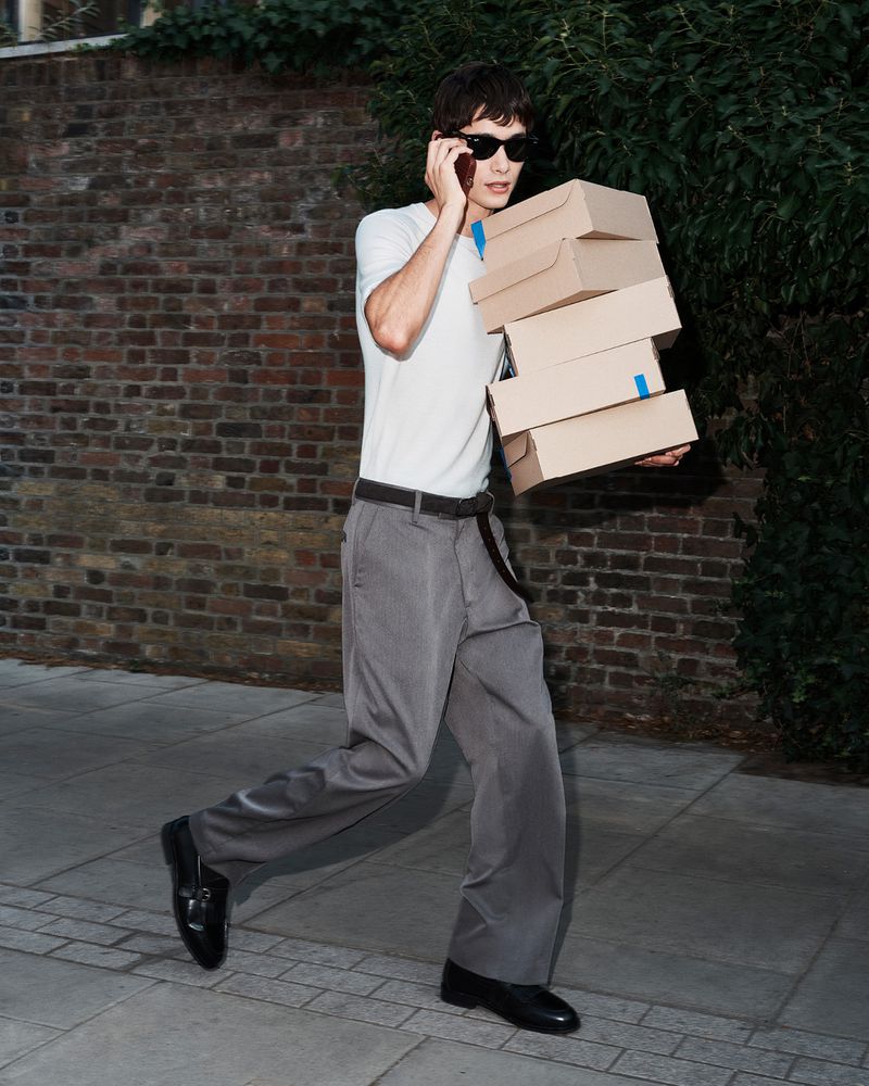 Man walking on a sidewalk carrying a stack of cardboard boxes while talking on a mobile phone