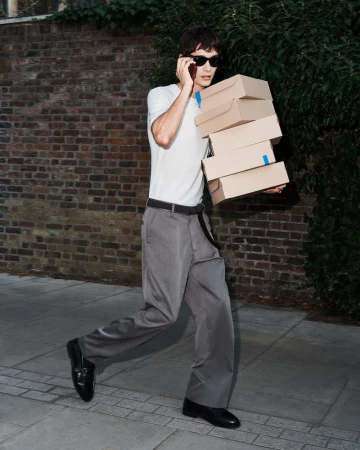 Man walking on a sidewalk carrying a stack of cardboard boxes while talking on a mobile phone