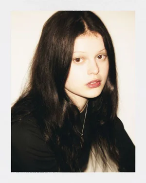 Portrait of a young woman with long dark hair wearing a black top against a plain light background