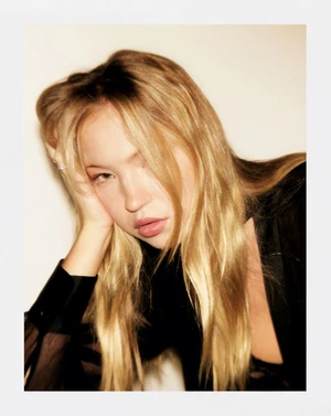 Portrait of blonde woman resting head on hand wearing black top against seamless background