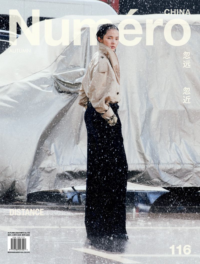 Model Xiao Wen Ju in a tan jacket and dark trousers standing outdoors amidst falling snow for Numero China.
