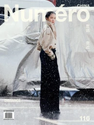 Model Xiao Wen Ju in a tan jacket and dark trousers standing outdoors amidst falling snow for Numero China.