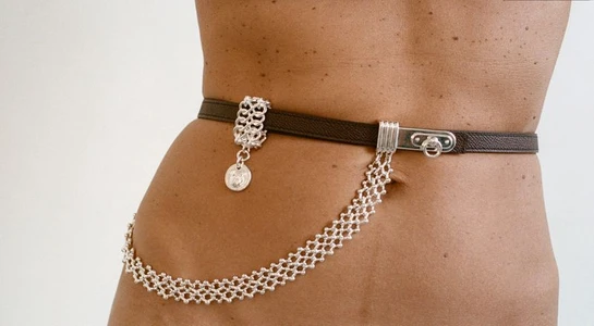 Close-up of a model wearing a brown leather belt with silver chain details against a white background.