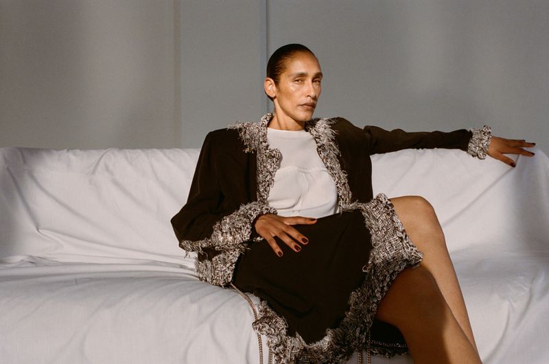 Model seated on a white couch wearing a dark tweed-trimmed coat and white top for Vogue Czechoslovakia.