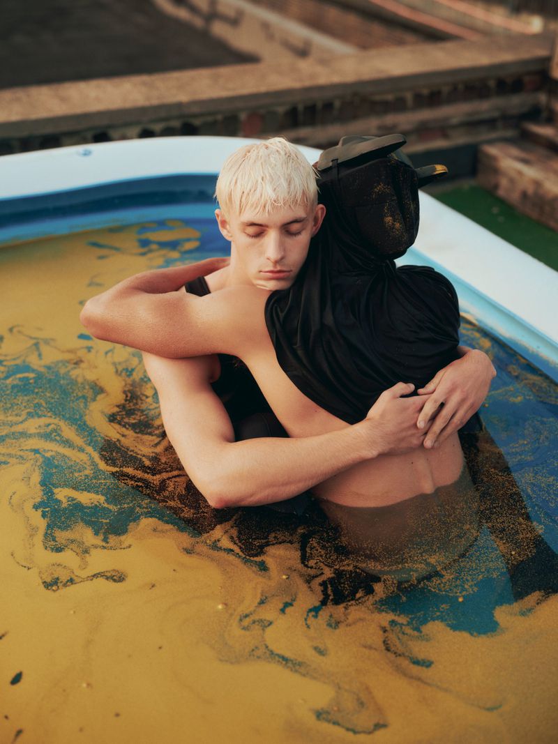 Two people embracing while partially submerged in a blue pool with murky yellow water