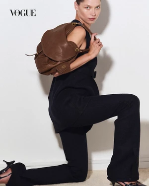 Model Hana Jirickova holding a brown leather bag, wearing black attire against a plain white studio backdrop.