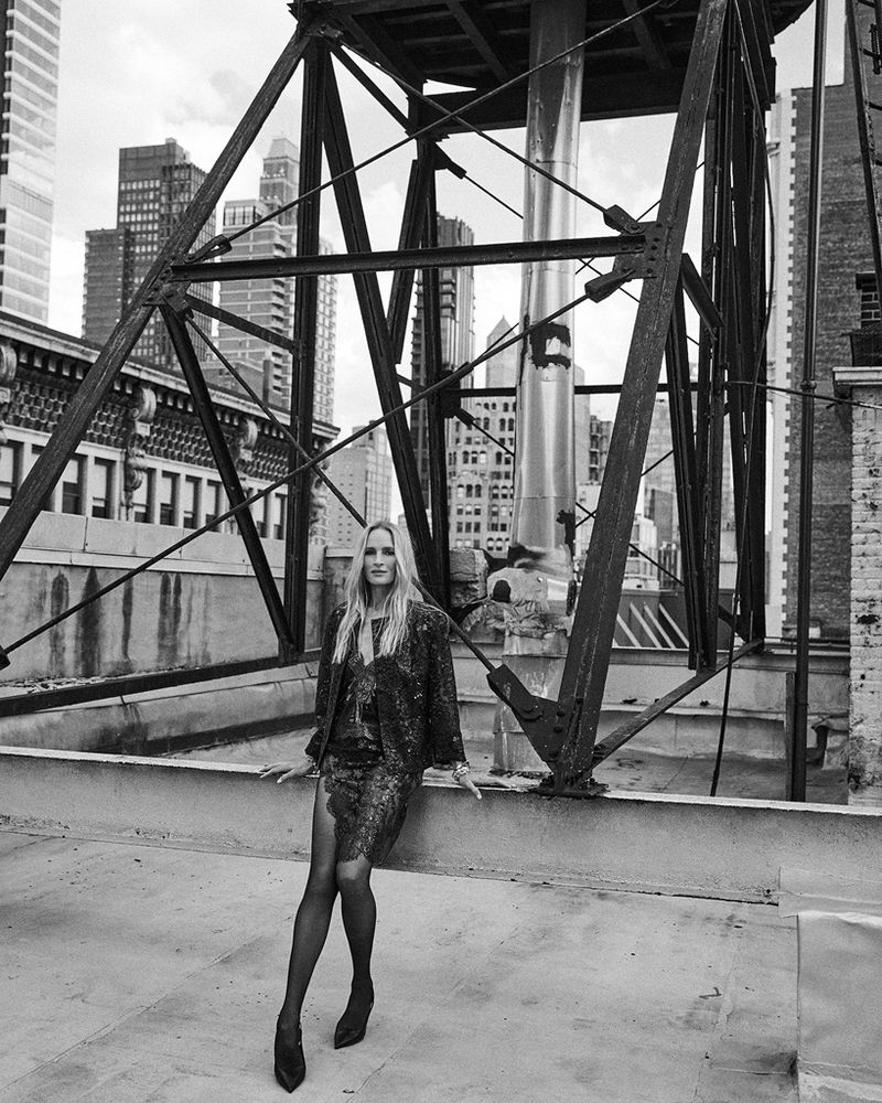 Black and white editorial portrait of Uma Thurman posing on a rooftop with structural steel framing and city skyline.