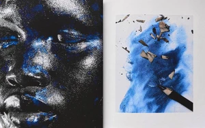 Close-up of a model's face with metallic blue highlights next to an open book showing blue pencil sketches and wood shavings