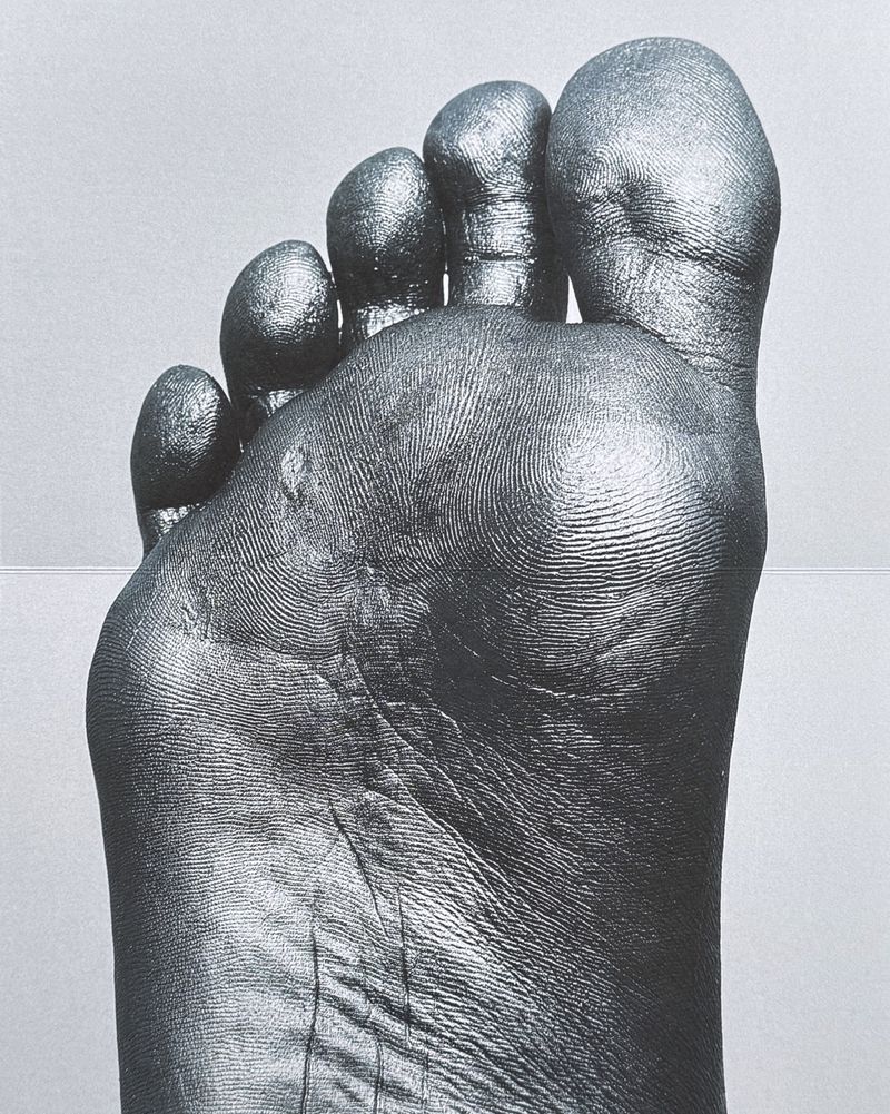 Close-up monochromatic photograph focusing on the sole of a bare foot, highlighting detailed skin texture and fingerprints.