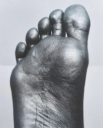 Close-up monochromatic photograph focusing on the sole of a bare foot, highlighting detailed skin texture and fingerprints.