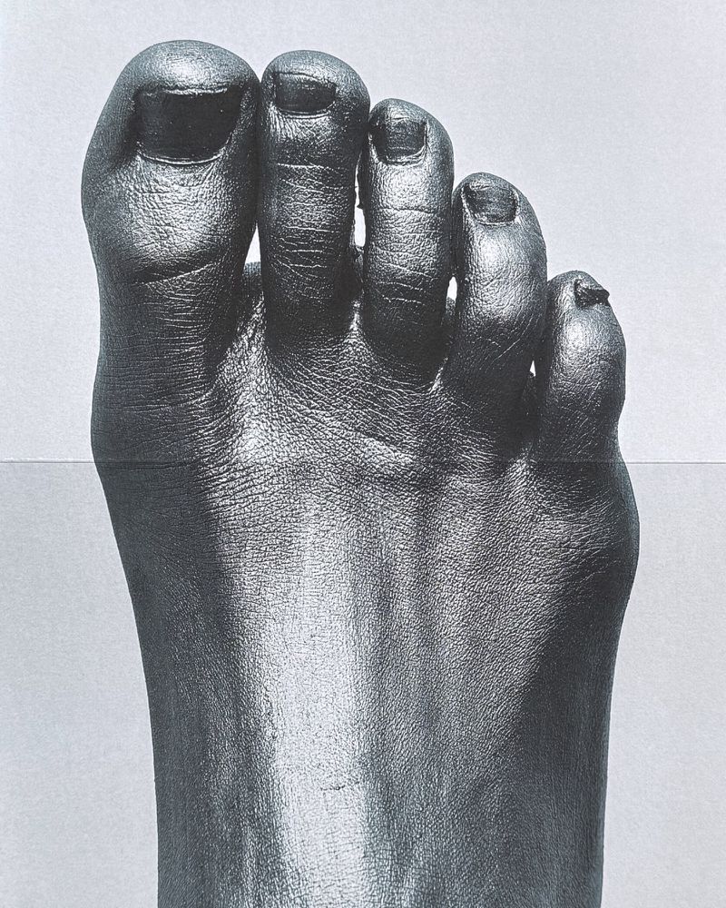Close-up macro shot of a human foot covered entirely in dark metallic or painted pigment against a plain background.