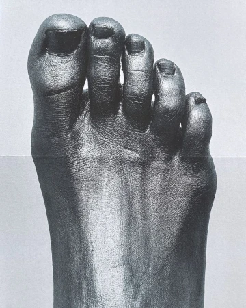 Close-up macro shot of a human foot covered entirely in dark metallic or painted pigment against a plain background.