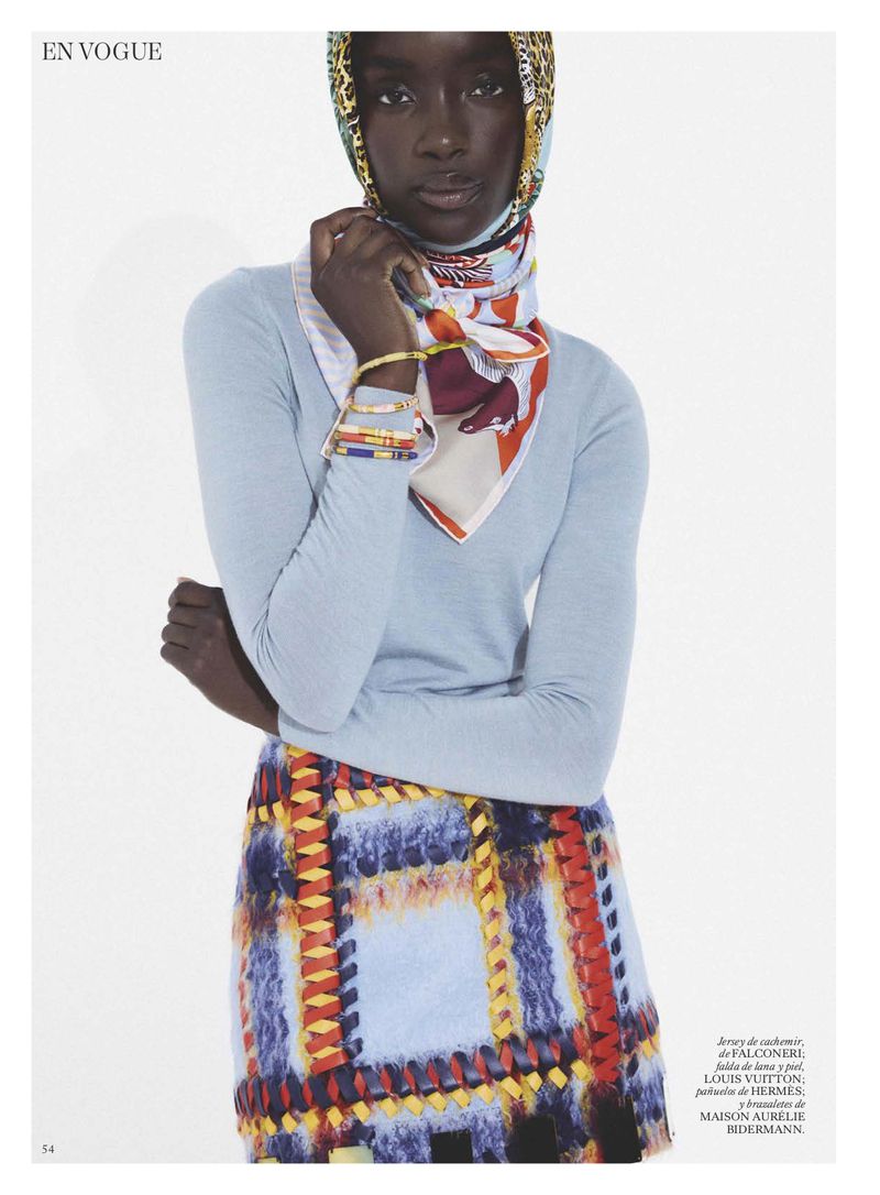 Model Maty Fall wearing a patterned headscarf, light blue top, and plaid skirt against a plain background