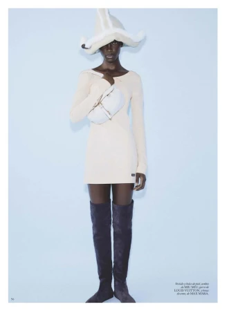 Model Maty Fall wearing cream dress, thigh-high boots, and sculptural hat holding a bag for Vogue Espana