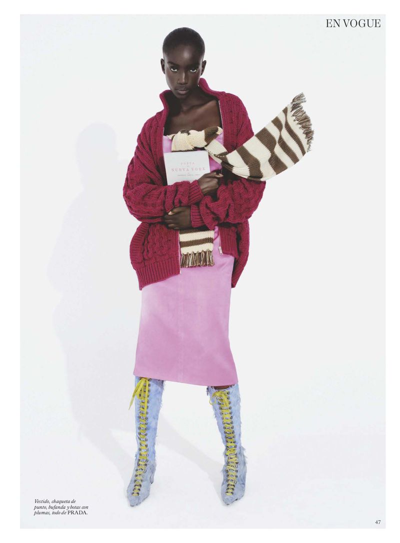 Model Maty Fall wearing a pink dress, red cardigan, and striped scarf holding a book against a white background