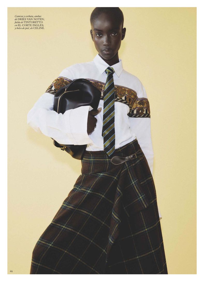 Model Maty Fall wearing patterned white shirt and plaid skirt holding a black handbag against a yellow backdrop for Vogue Espana